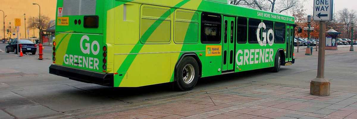 A green-colored electric bus in downtown Minneapolis advertising "Go GREENER"