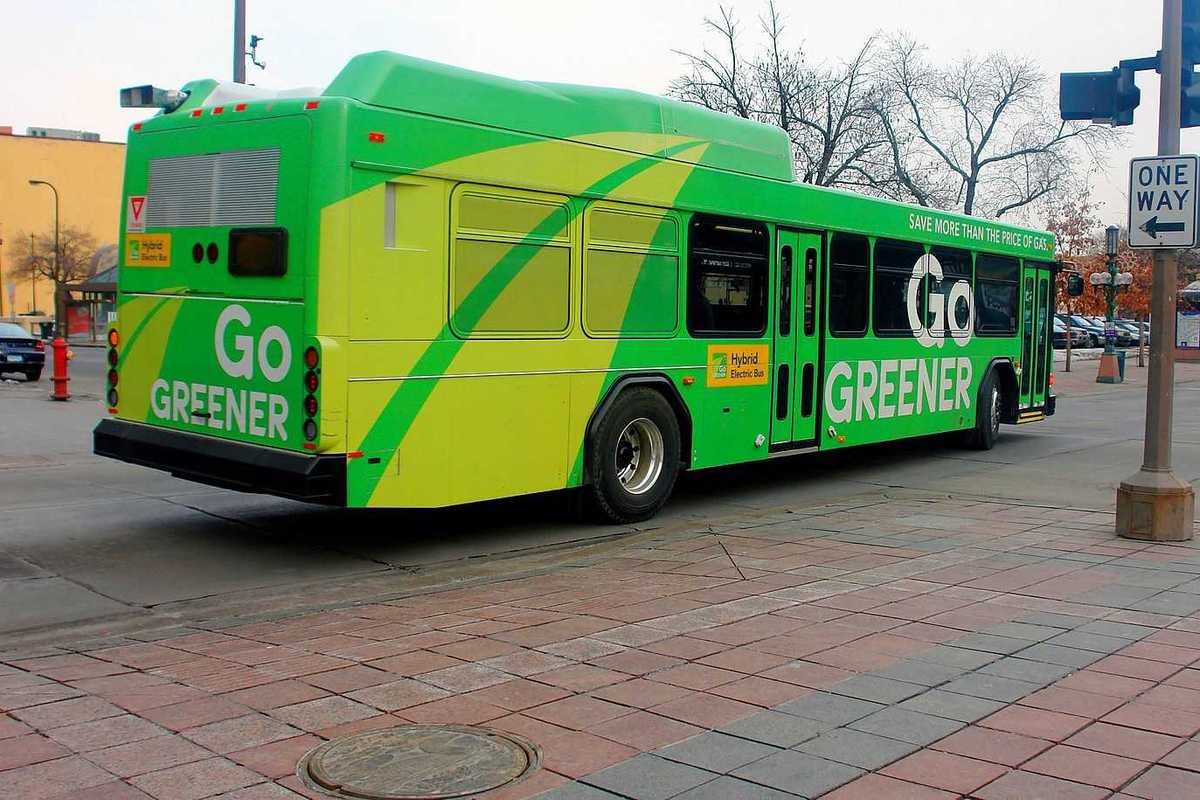 A green-colored electric bus in downtown Minneapolis advertising "Go GREENER"