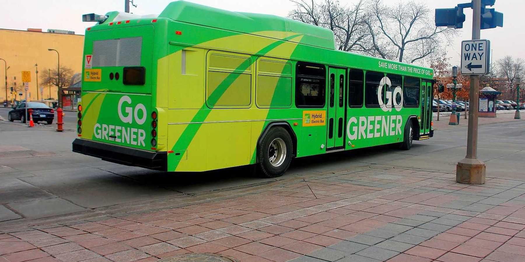 A green-colored electric bus in downtown Minneapolis advertising "Go GREENER"
