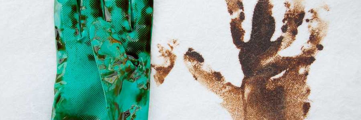 A green rubber glove covered in oil next to an oily handprint