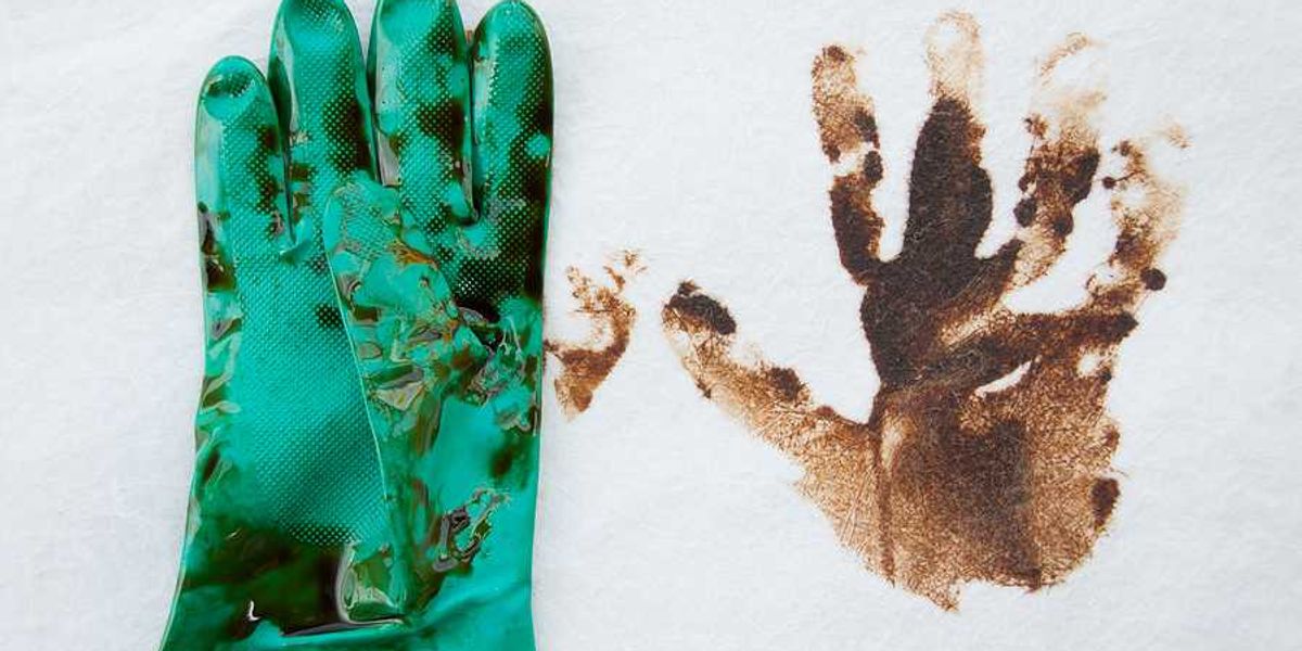 A green rubber glove covered in oil next to an oily handprint