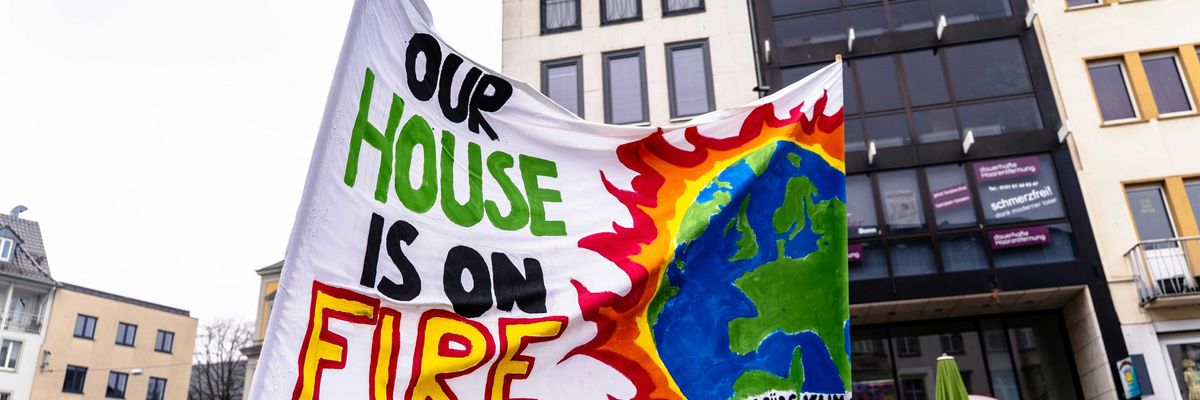 A group of climate protesters holding a sign that says our house is on fire.