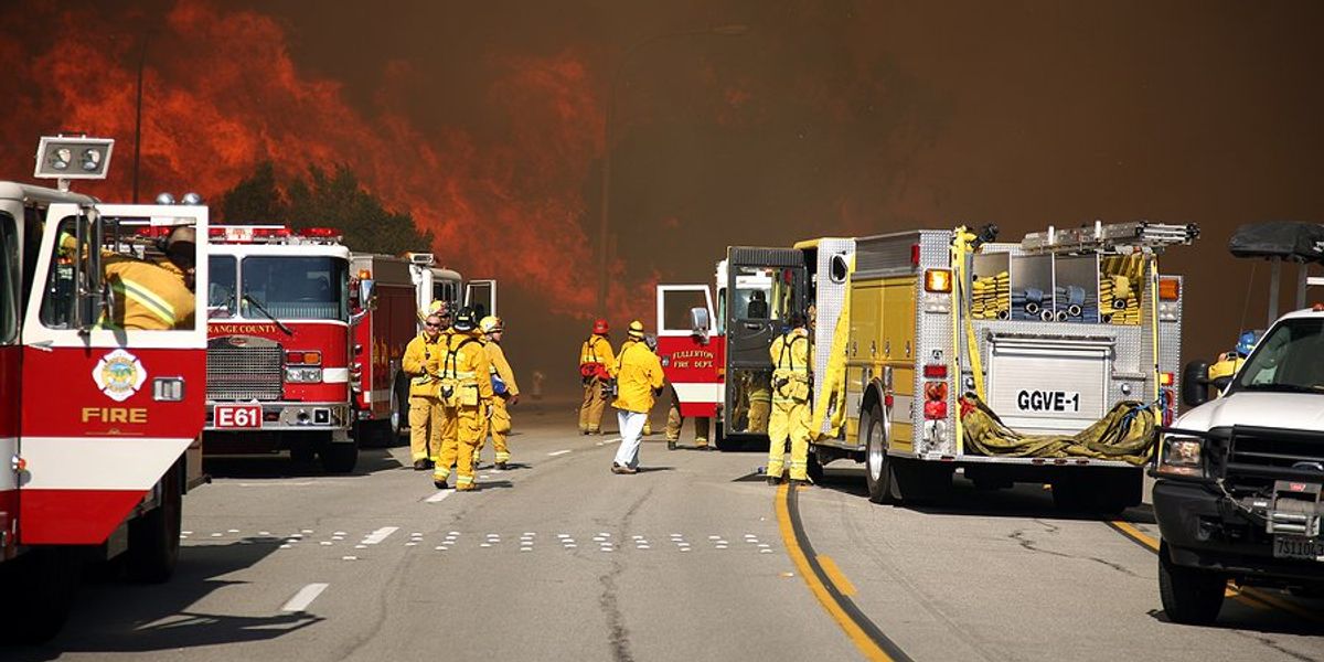 A group of firetrucks and firefighters face a burning hillside.