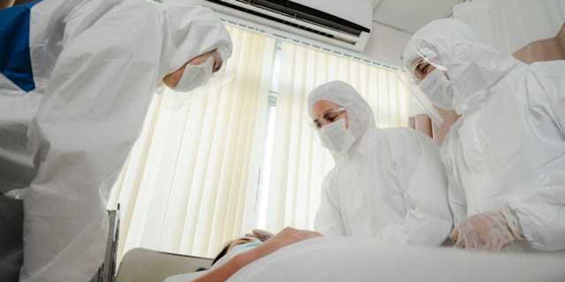 A group of masked health professionals standing over a patient's bed