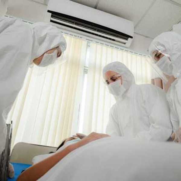 A group of masked health professionals standing over a patient's bed