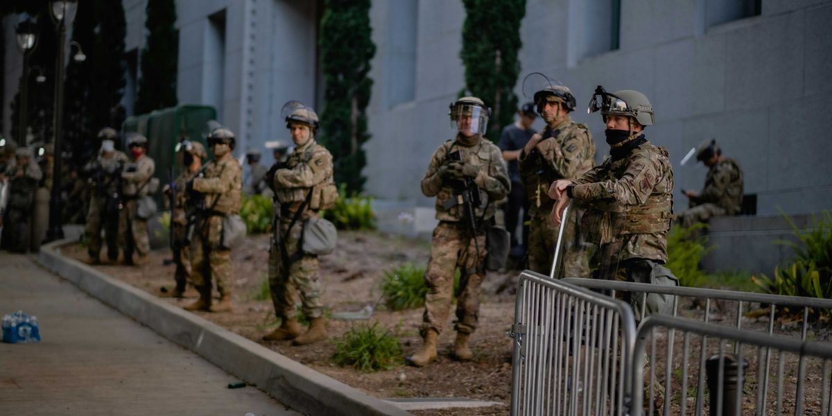 a group of national guard on a sidewalk in front of a building.