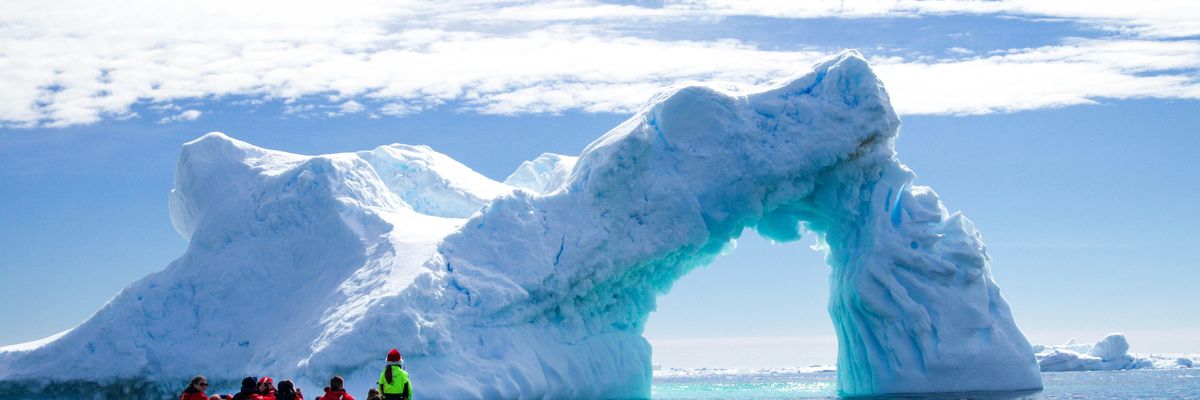 a group of people in a small boat in front of an iceberg.