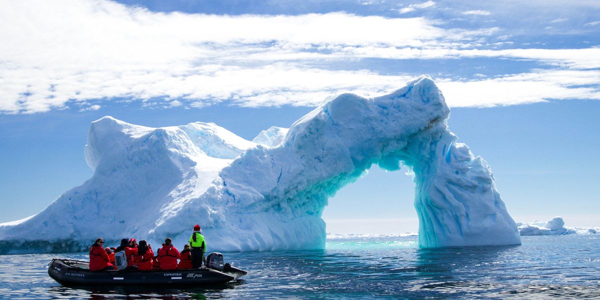 a group of people in a small boat in front of an iceberg.