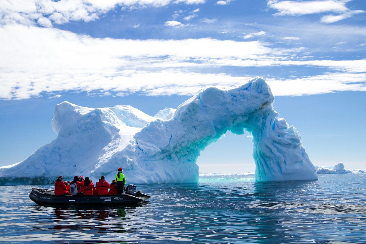 a group of people in a small boat in front of an iceberg.