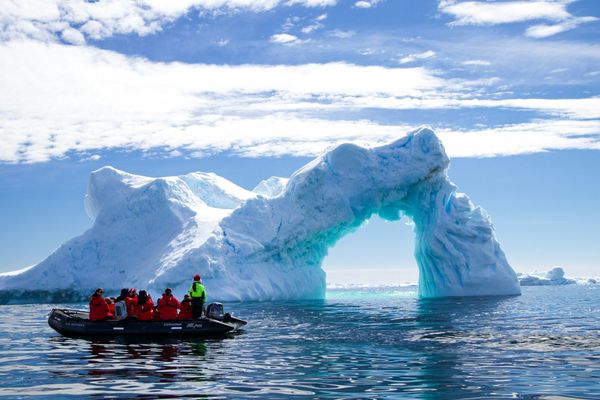 a group of people in a small boat in front of an iceberg.