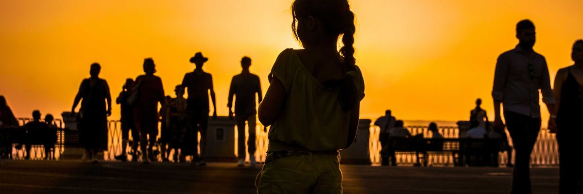 A group of people silhouetted against an orange sun-tinged sky