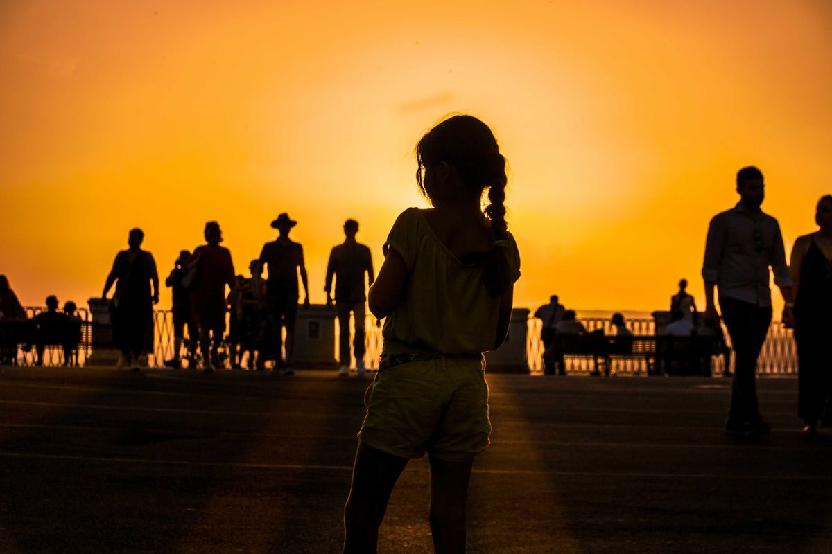 A group of people silhouetted against an orange sun-tinged sky