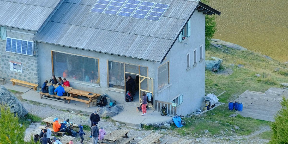 A group of people standing outside of a house with a body of water in background.