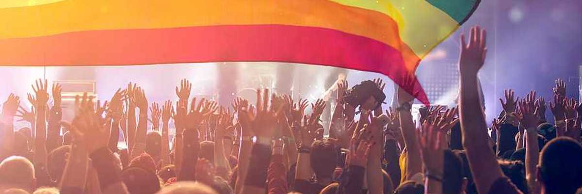 A group of people with their hands waving holding an LGBTQ flag in the air