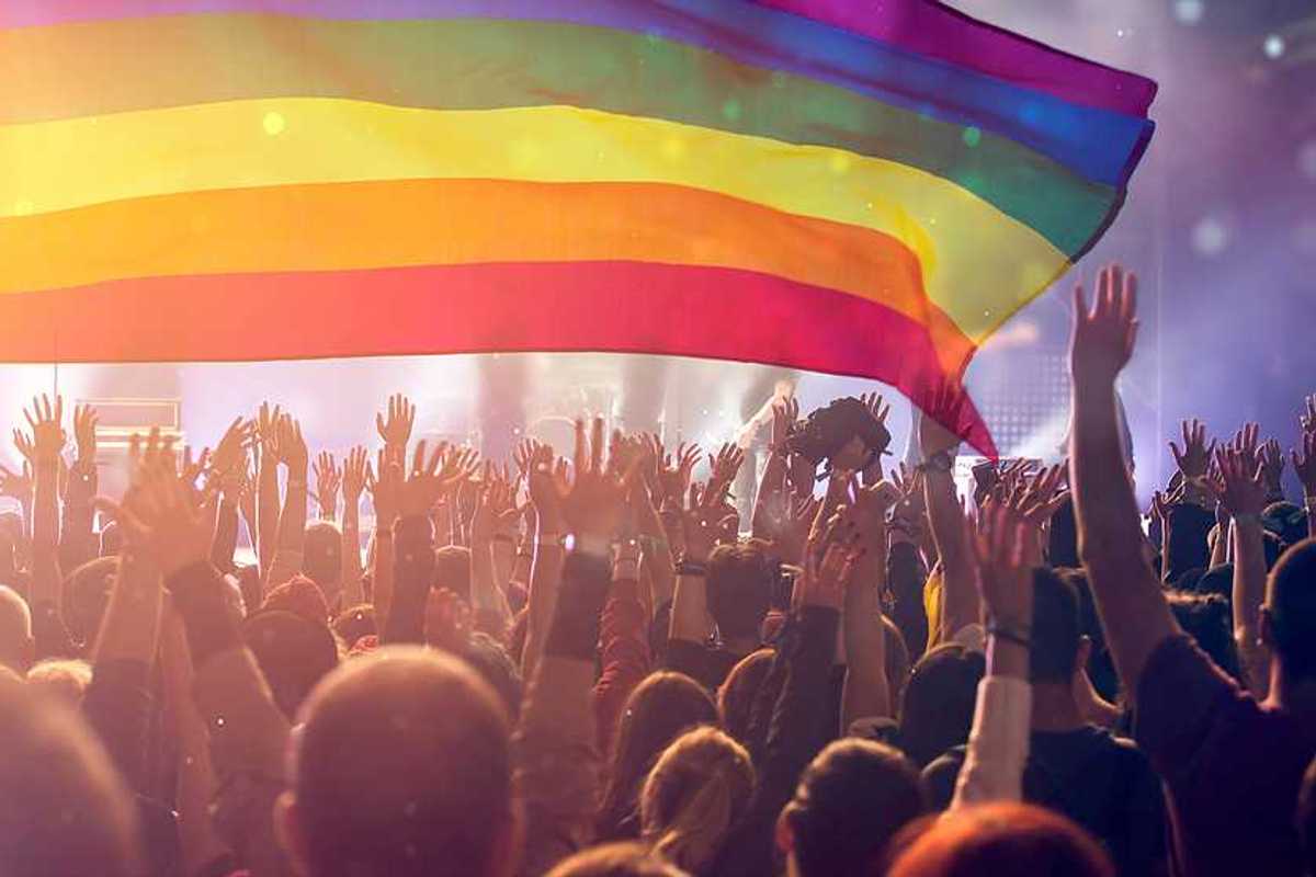 A group of people with their hands waving holding an LGBTQ flag in the air