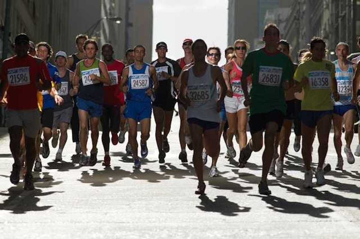A group of runners with numbered tags running on a city street