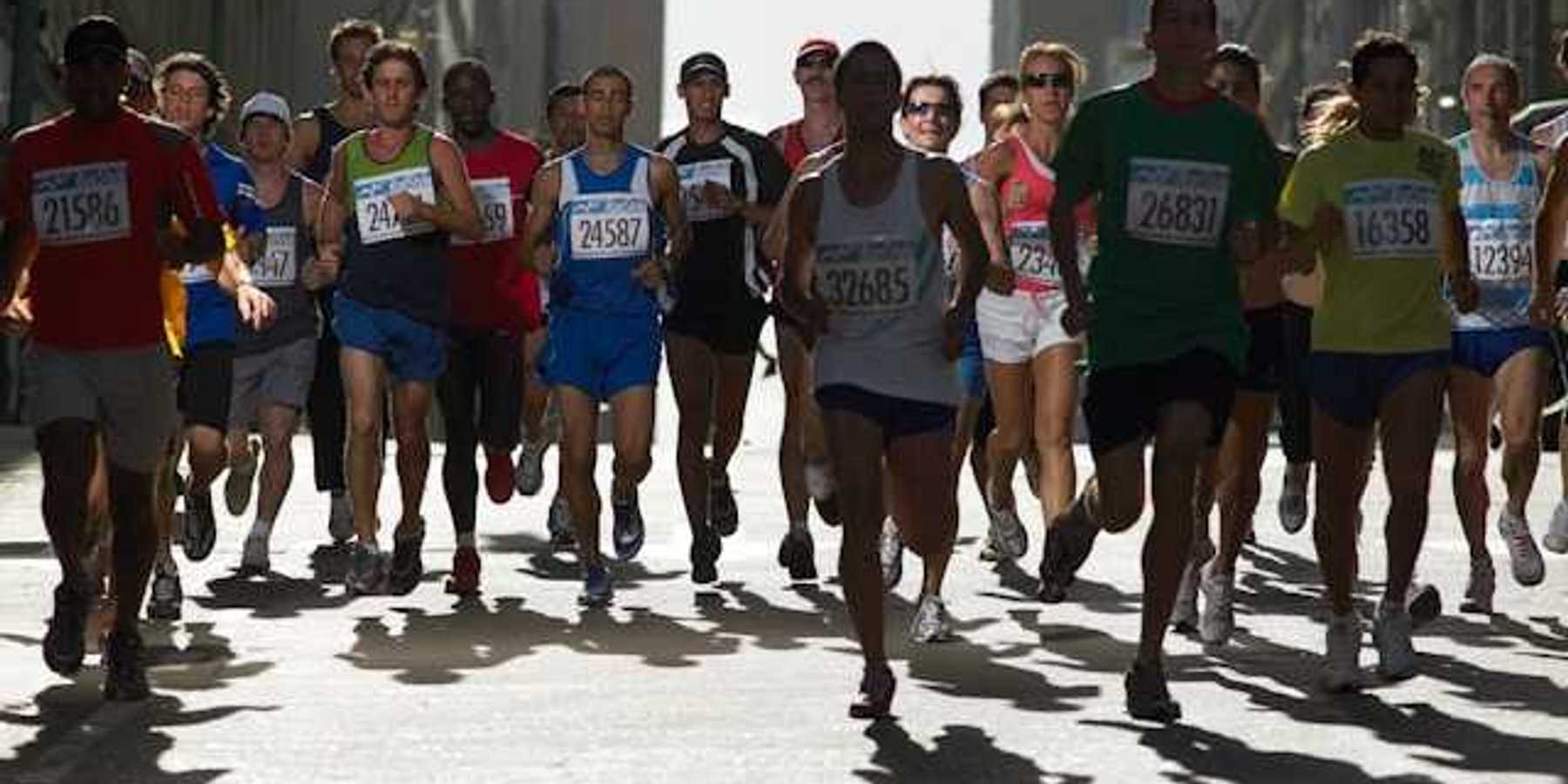 A group of runners with numbered tags running on a city street