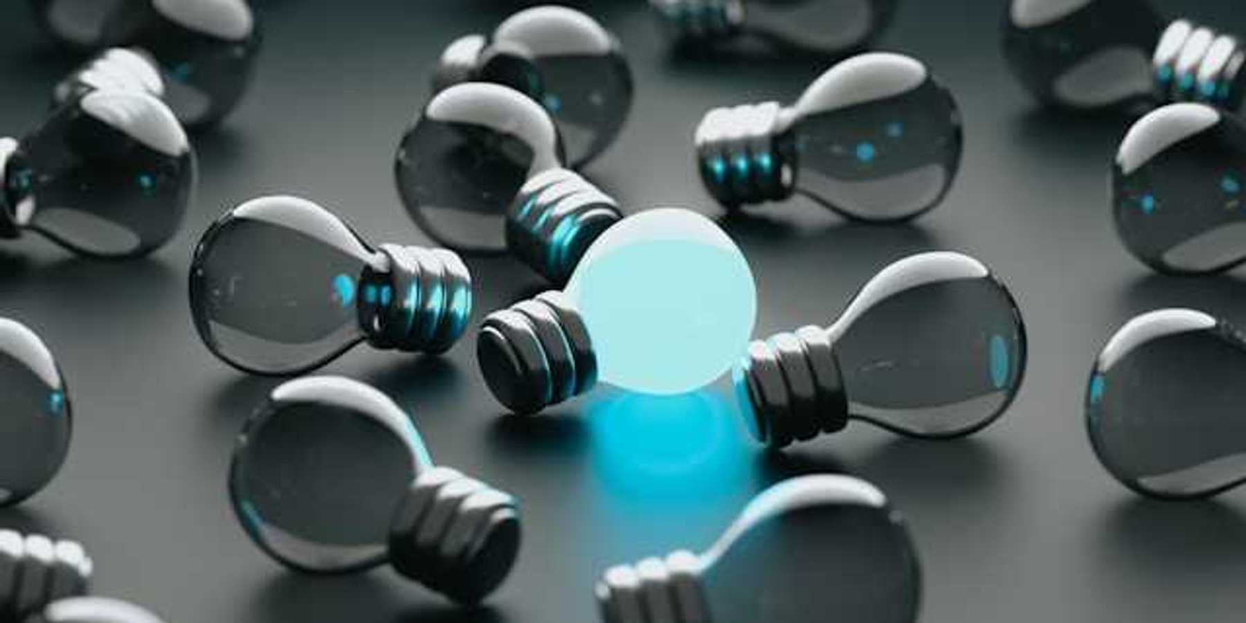 A group of unlit lightbulbs with one bulb glowing blue