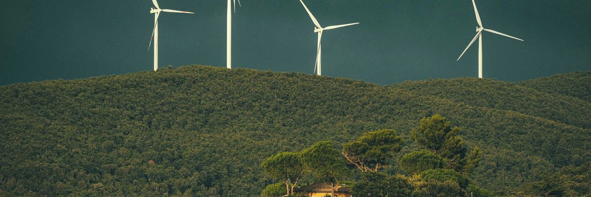 a group of wind turbines on top of a forested hill with dark clouds in background.
