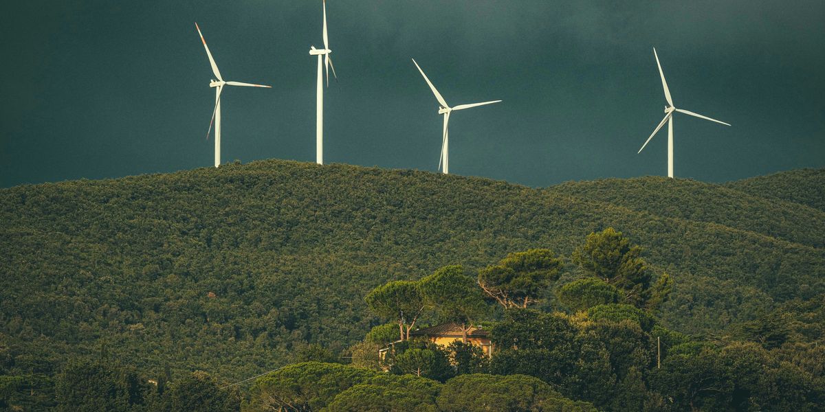 a group of wind turbines on top of a forested hill with dark clouds in background.