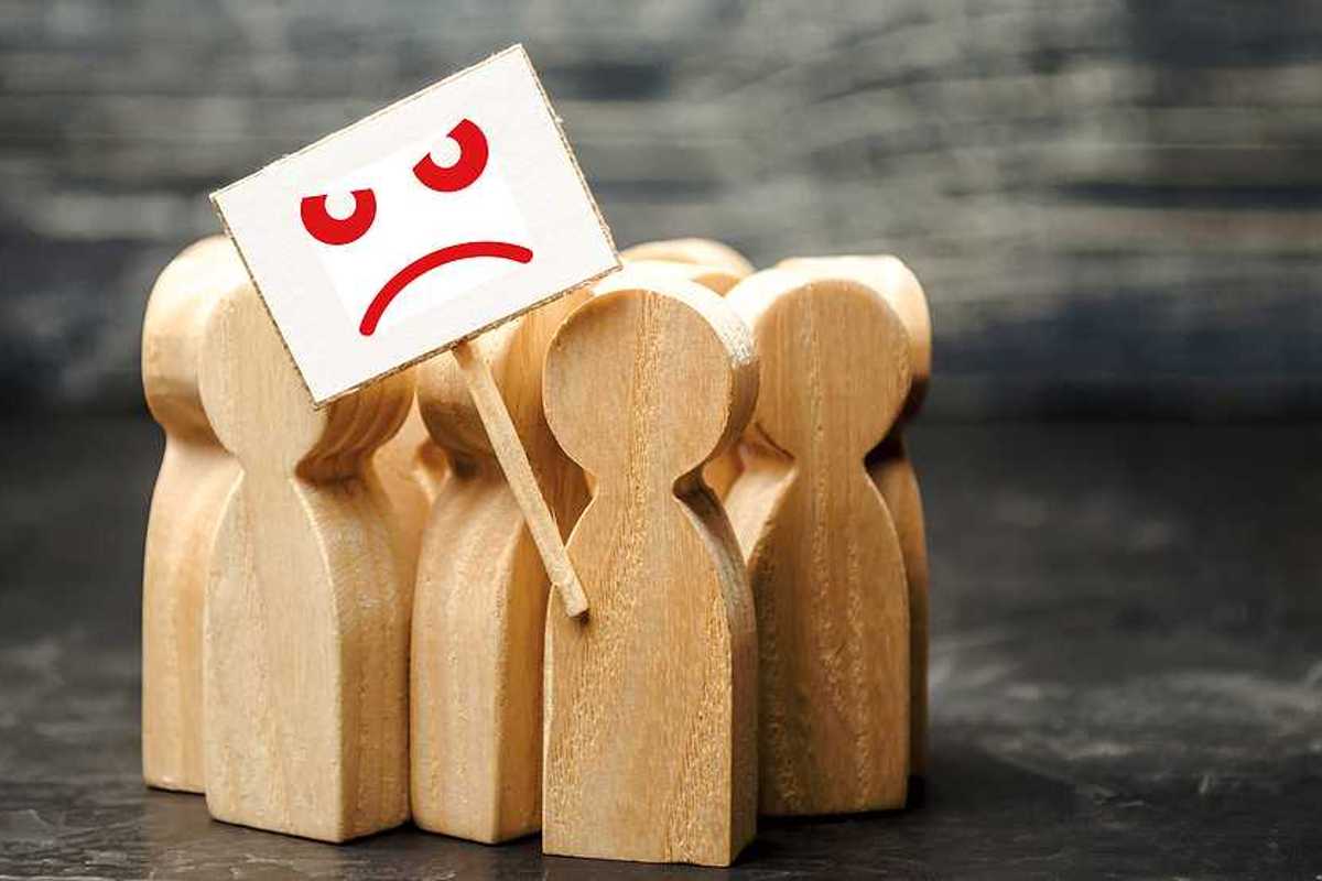 A group of wooden figures shaped like people with a protest sign with a sad face on it