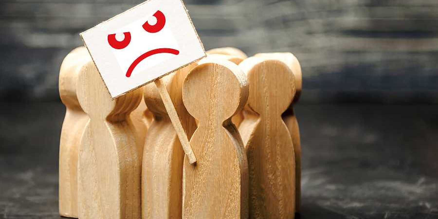 A group of wooden figures shaped like people with a protest sign with a sad face on it