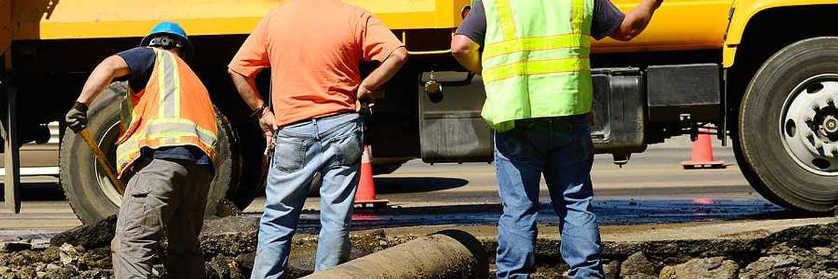A group of workers standing next to a yellow truck fixing a pipe