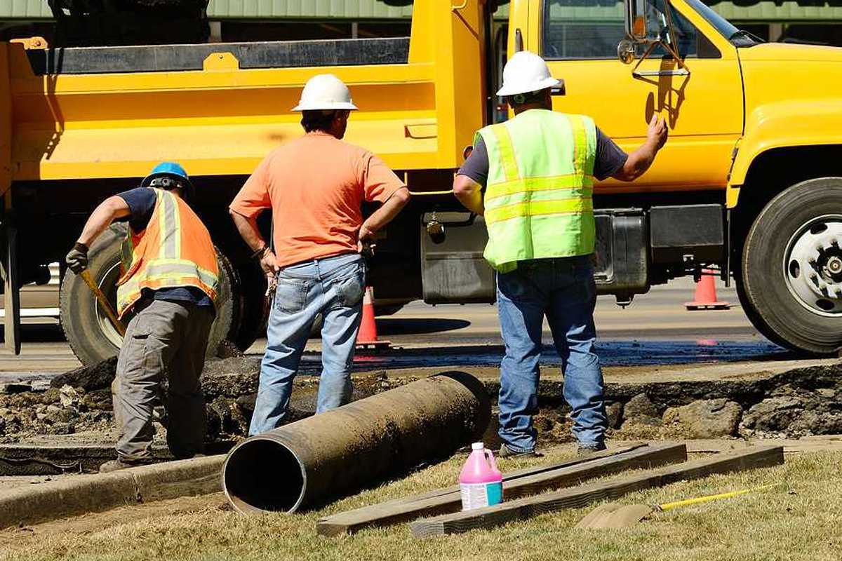 A group of workers standing next to a yellow truck fixing a pipe