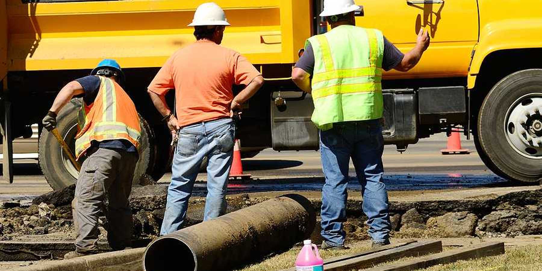 A group of workers standing next to a yellow truck fixing a pipe