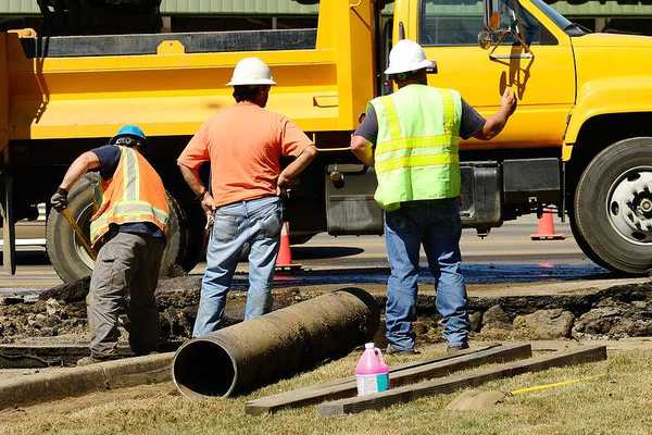 A group of workers standing next to a yellow truck fixing a pipe
