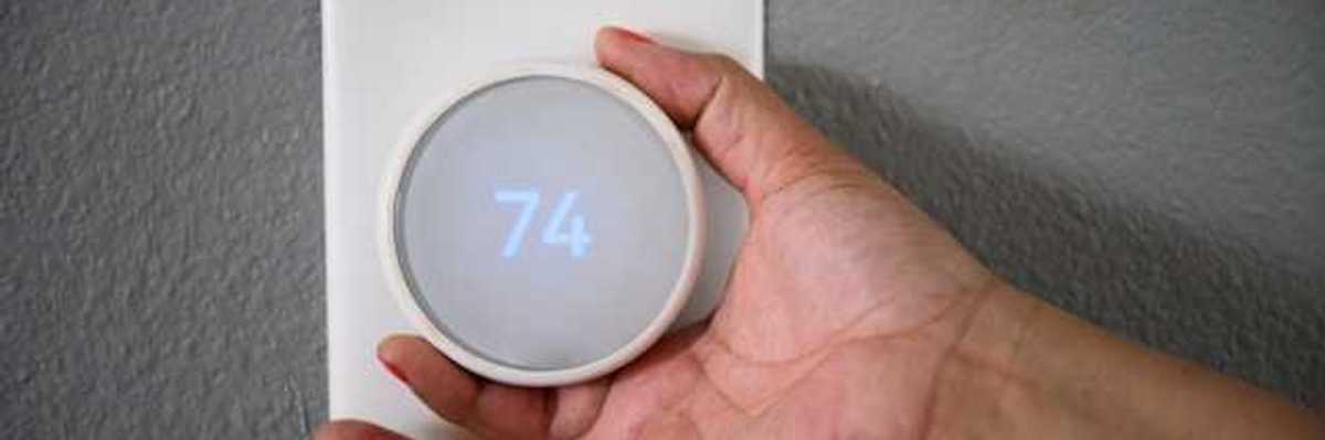 A hand adjusting the temperature on a wall thermostat