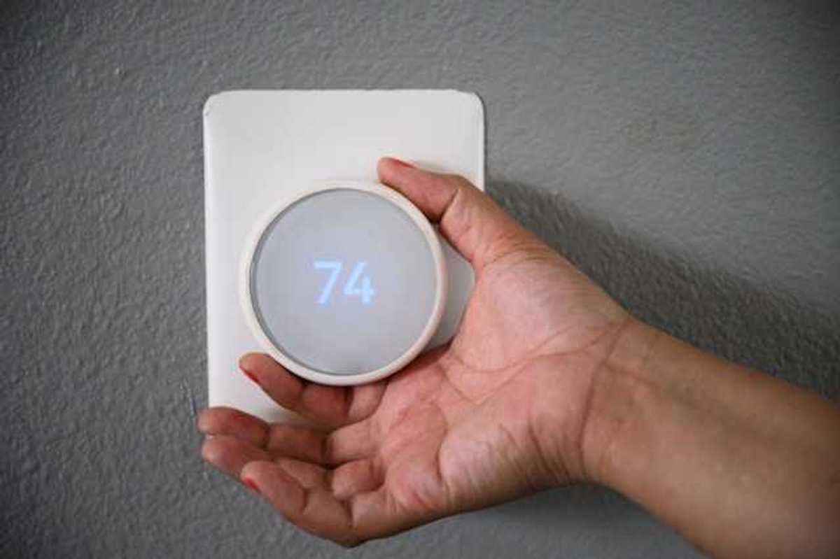 A hand adjusting the temperature on a wall thermostat