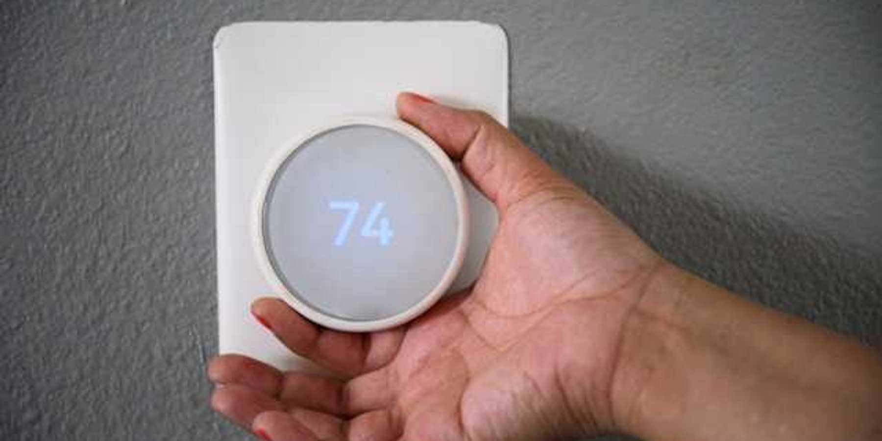 A hand adjusting the temperature on a wall thermostat