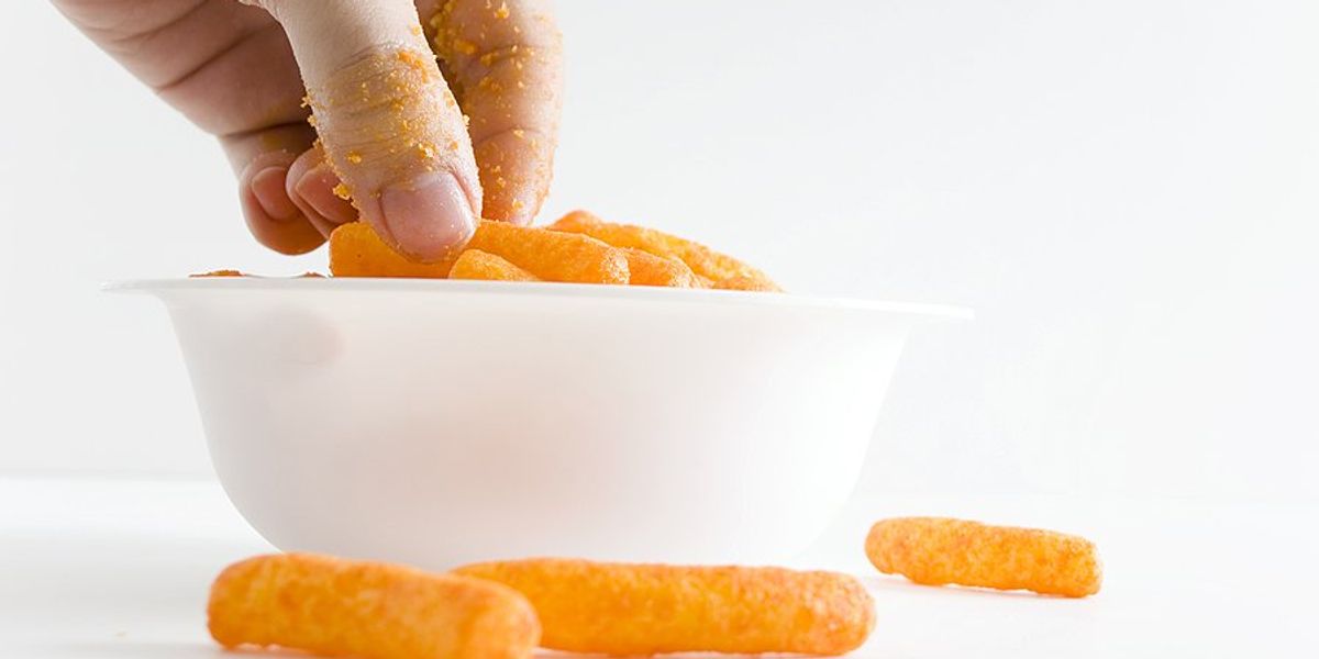 A hand reaching for cheese puffs in a white bowl