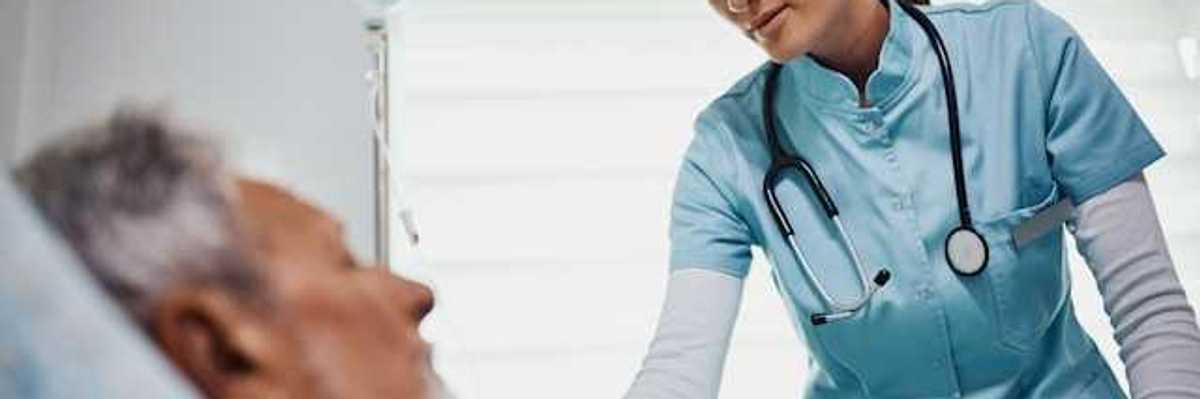 A health care professional wearing scrubs and a stethoscope leaning over an older patient in a bed