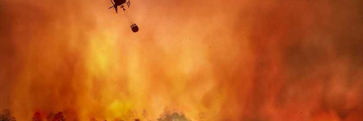 A helicopter dropping water onto a wildfire with burning trees in the background