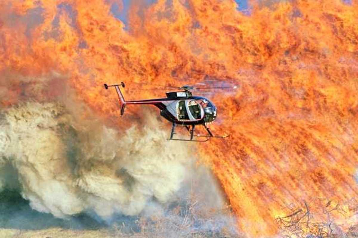 A helicopter flies over a burning field