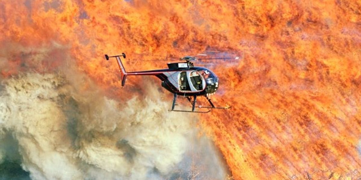 A helicopter flying above a wildfire in a dry environment.