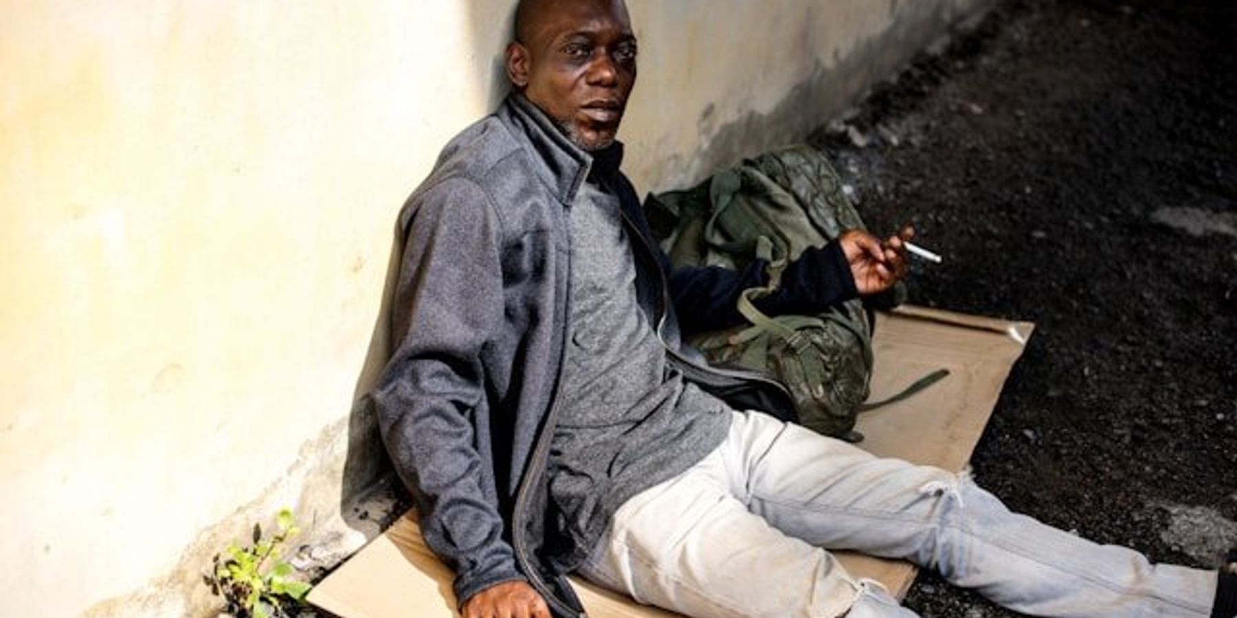 A homeless man sitting on the ground smoking a cigarette.