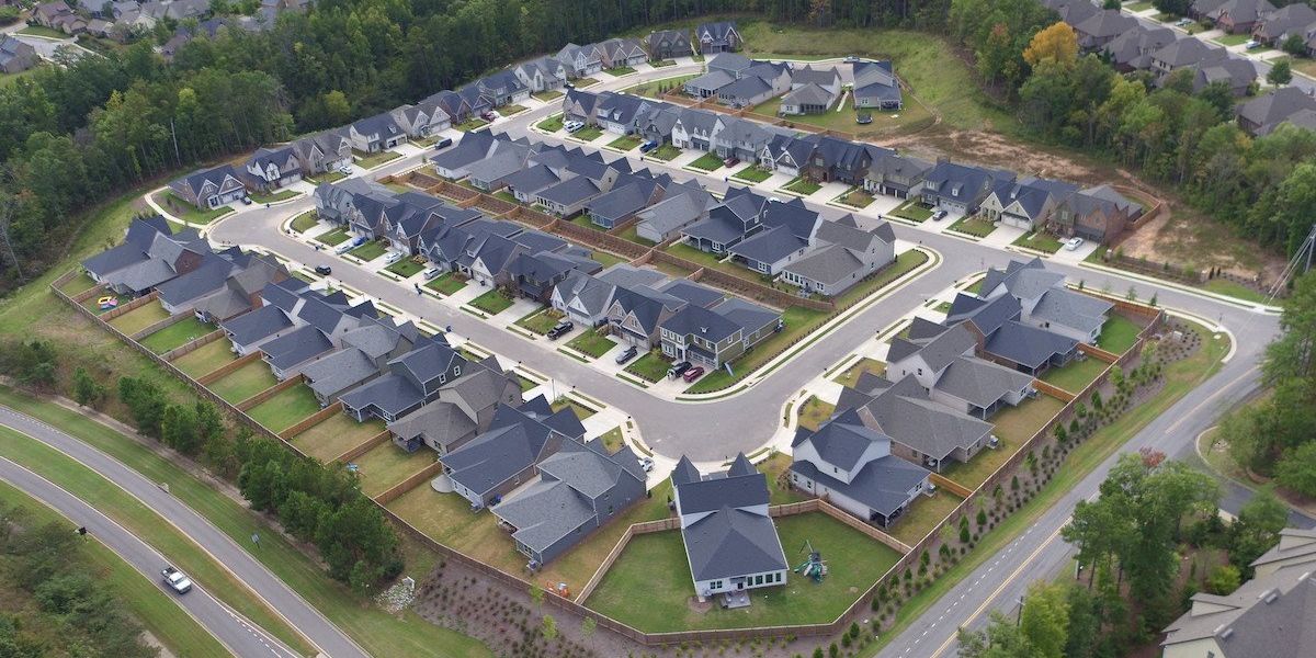 A housing subdivision built in a spiraling square shape and featuring renewable energy, surrounded by trees and roads.
