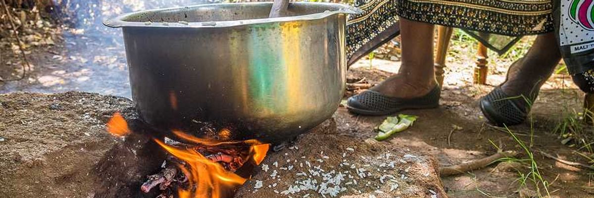 A kenyan woman cooking food in a large silver pot in the outdoors