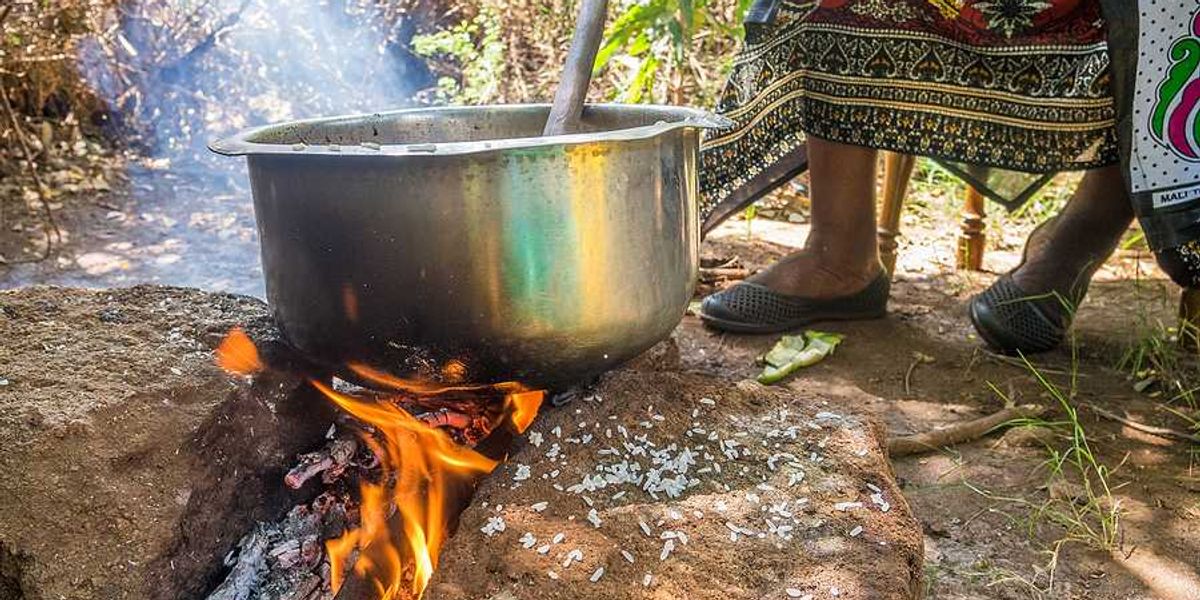 A kenyan woman cooking food in a large silver pot in the outdoors