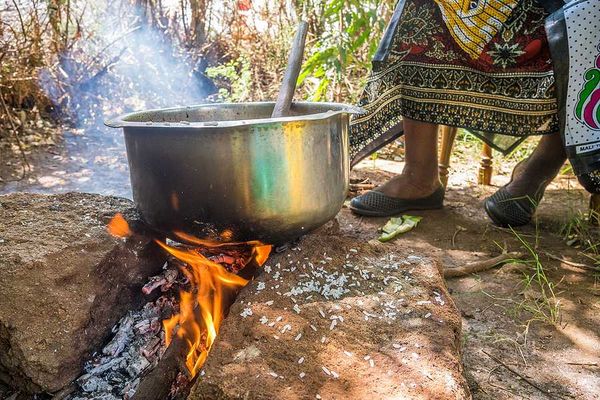 A kenyan woman cooking food in a large silver pot in the outdoors
