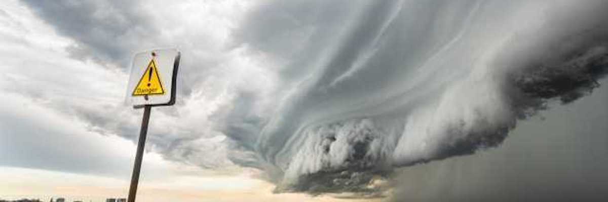 A large storm front approaching a beach from the ocean, with a danger sign in the foreground