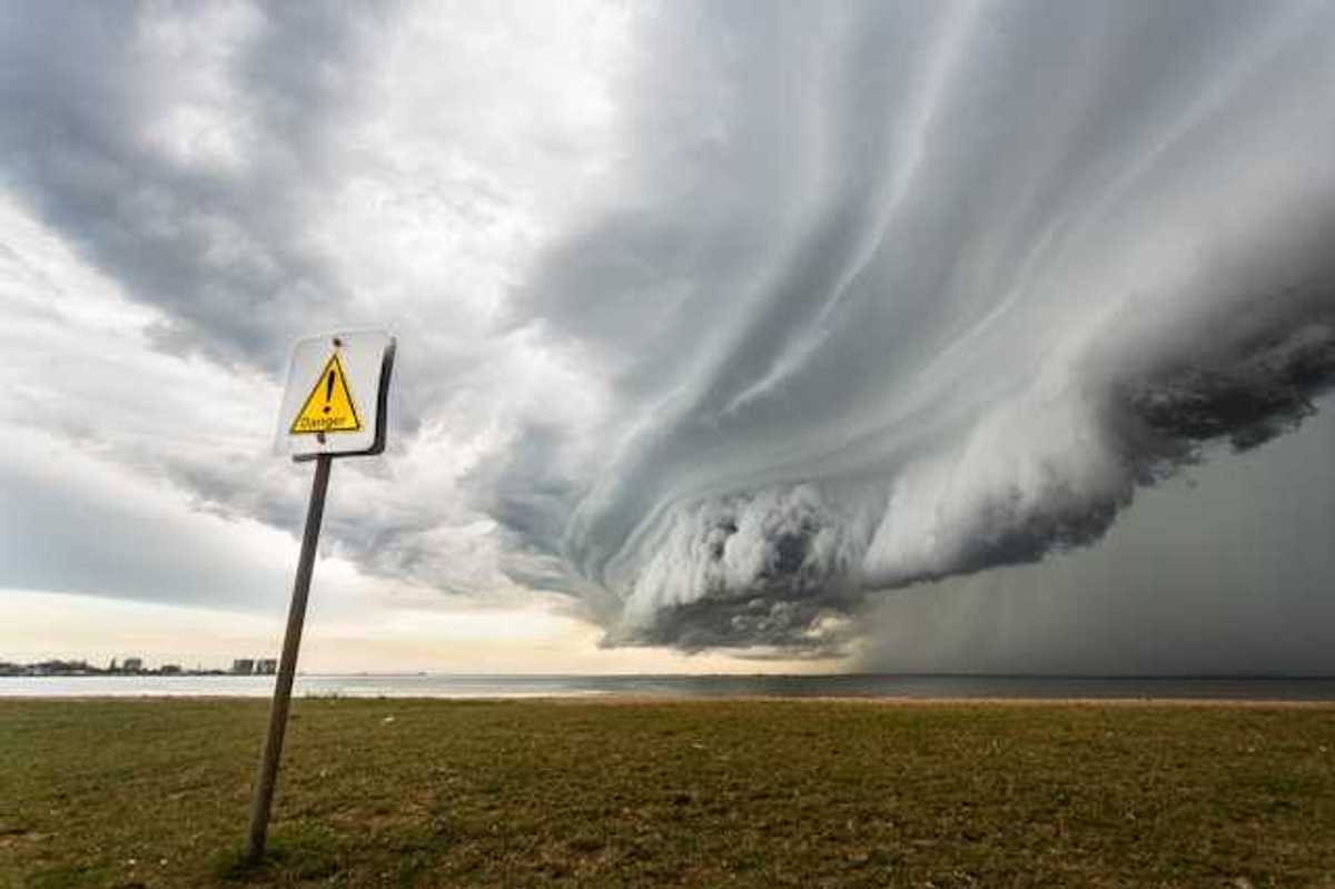 A large storm front approaching a beach from the ocean, with a danger sign in the foreground