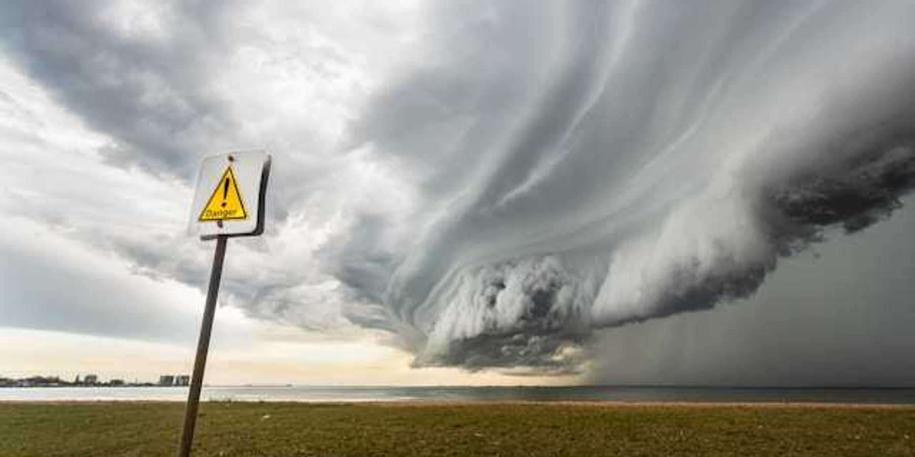 A large storm front approaching a beach from the ocean, with a danger sign in the foreground