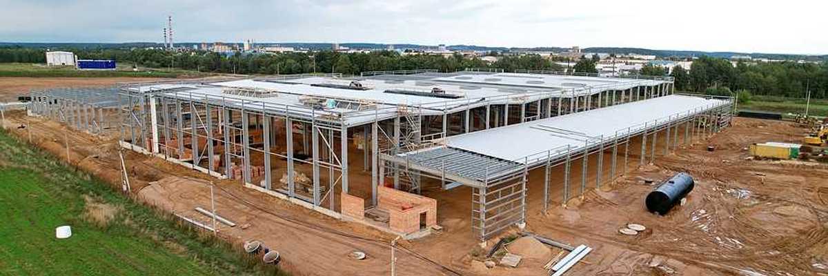 A large warehouse under construction with green fields and a town in the distance