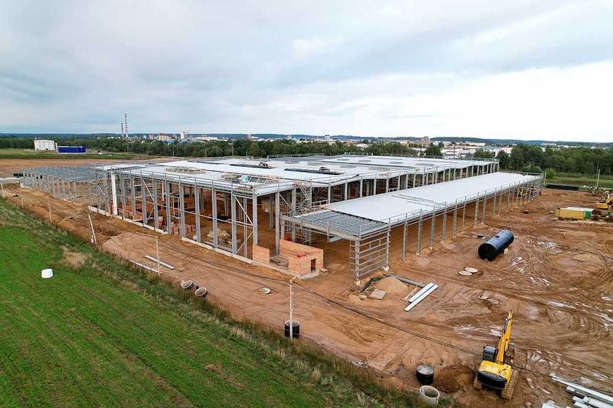 A large warehouse under construction with green fields and a town in the distance