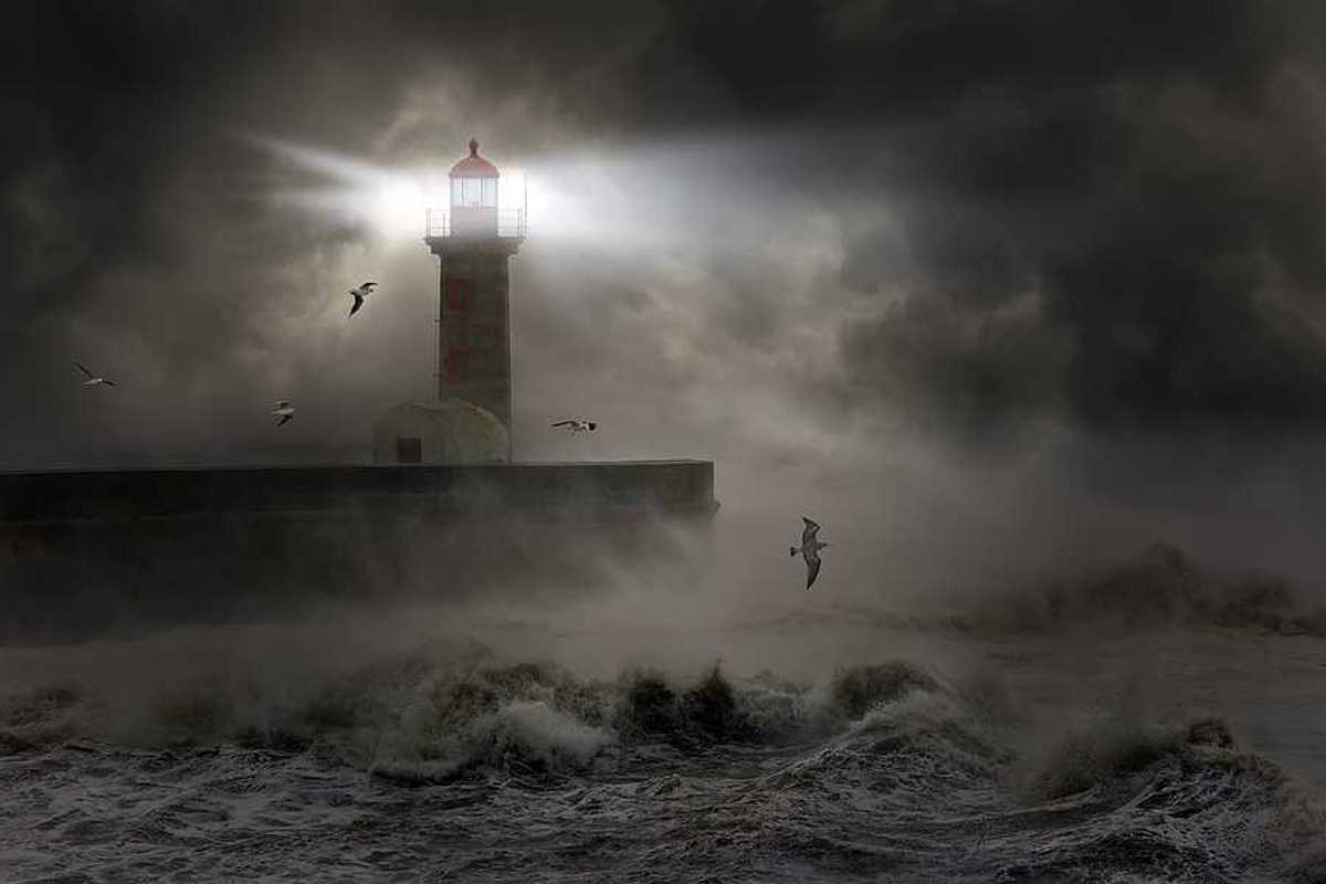 A lighthouse at the end of a promontory during a strong storm
