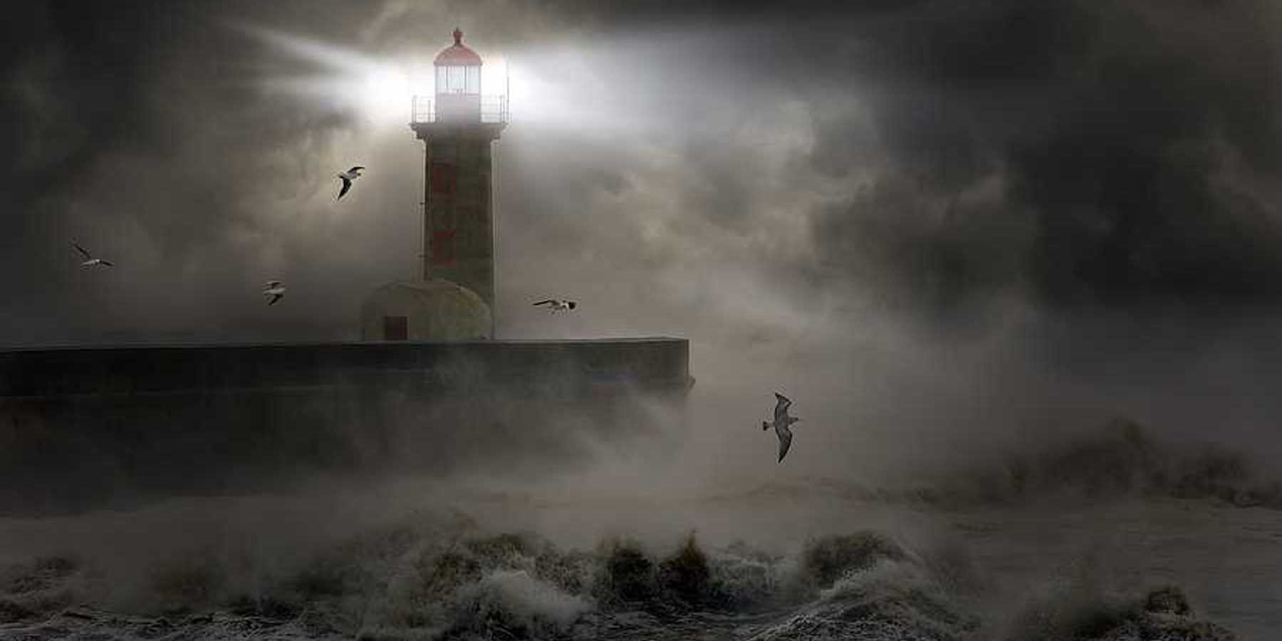 A lighthouse at the end of a promontory during a strong storm